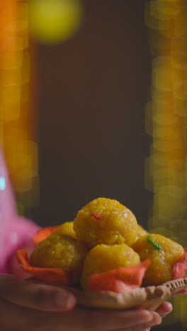 Vertical-Video-Close-Up-Of-Woman-Celebrating-Festival-Of-Diwali-Holding-Dish-Of-Ladoo